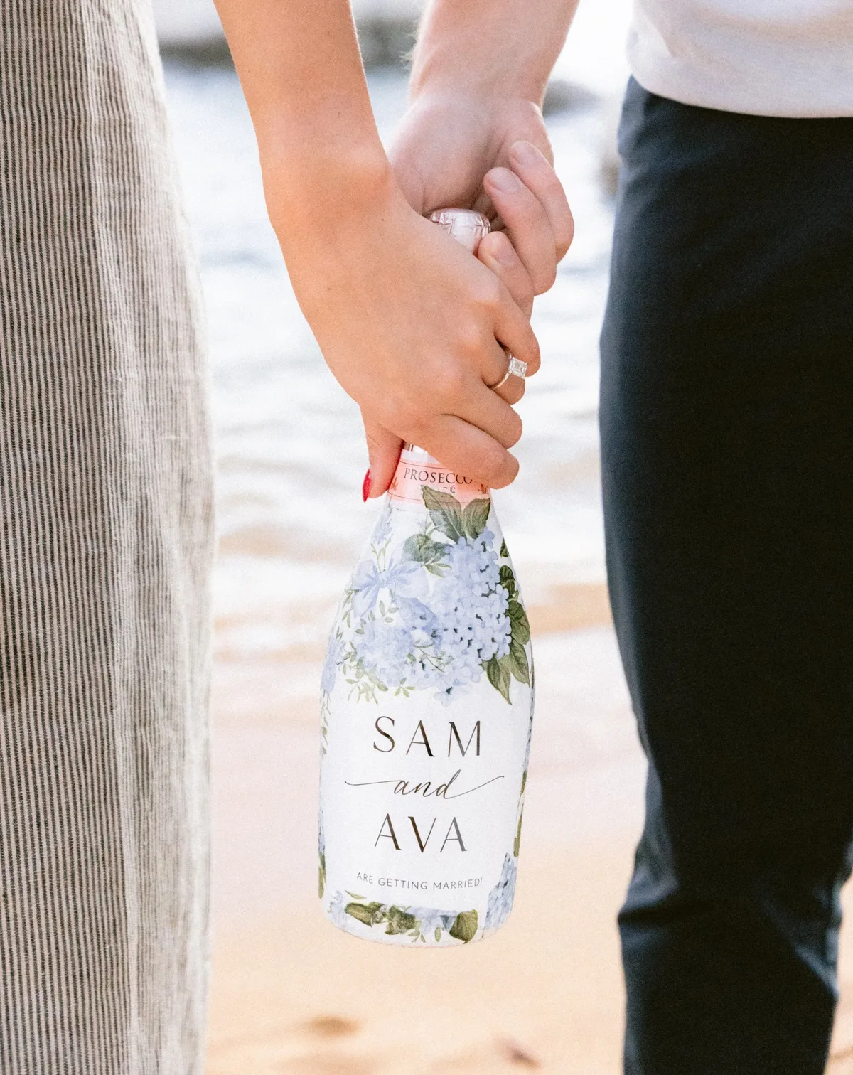 Couple holding a personalized engagement bottle by the lake