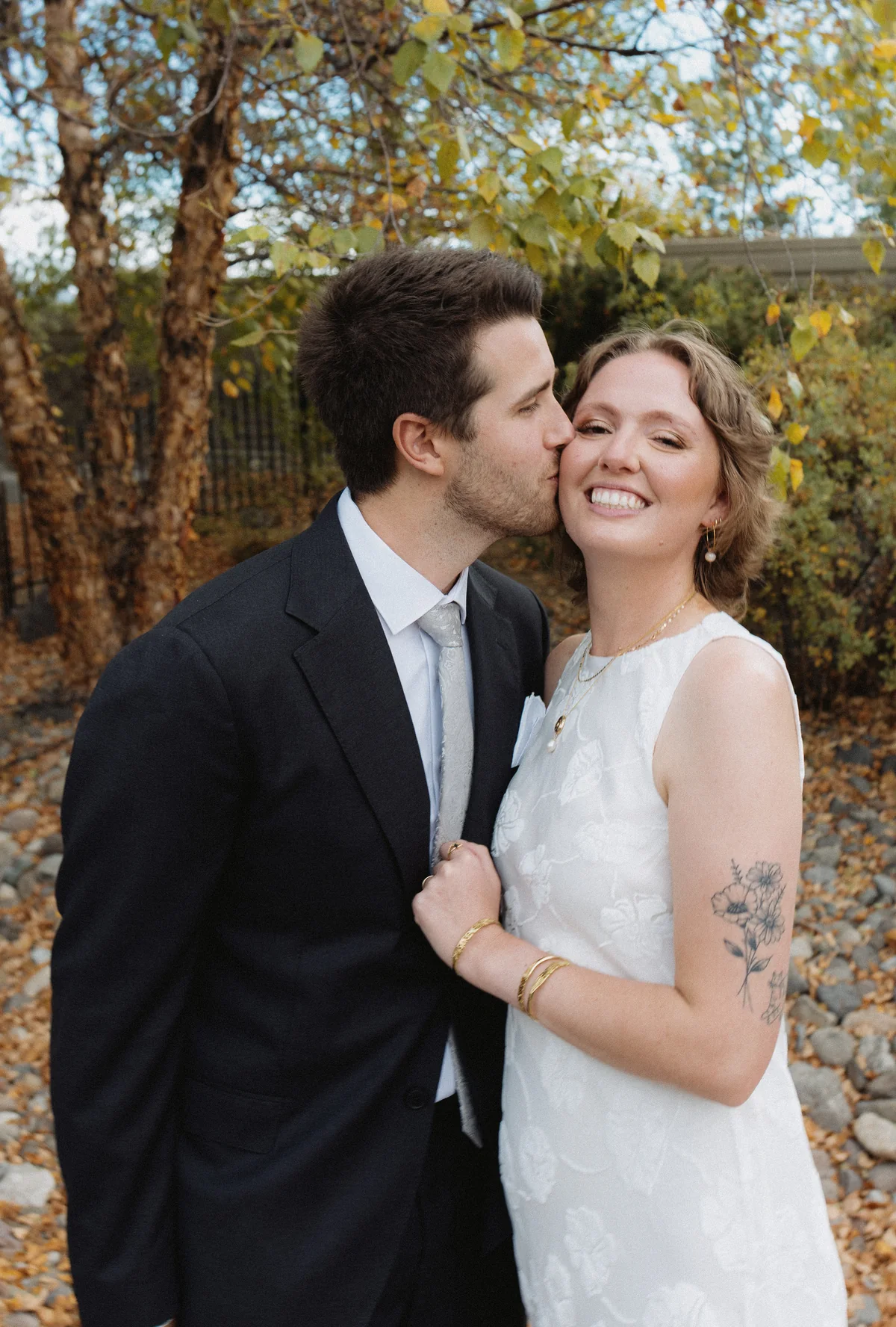 Groom kissing the bride on the cheek under golden fall trees