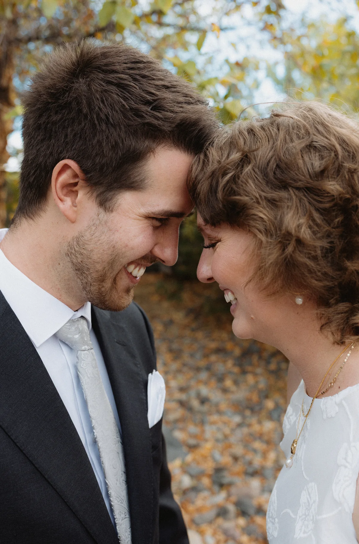 Bride and groom forehead to forehead, laughing, among autumn leaves
