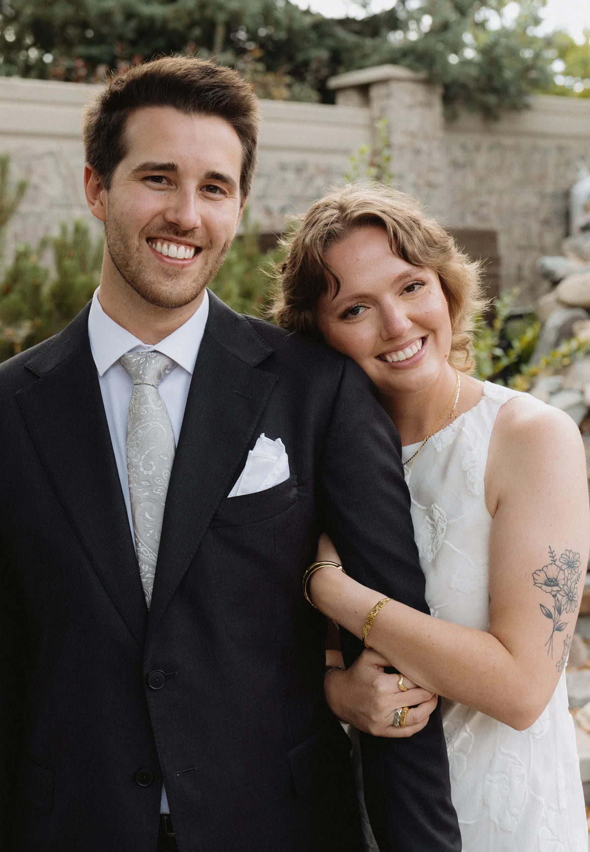 Groom smiling at the camera as the bride leans her head on his shoulder in a stone garden