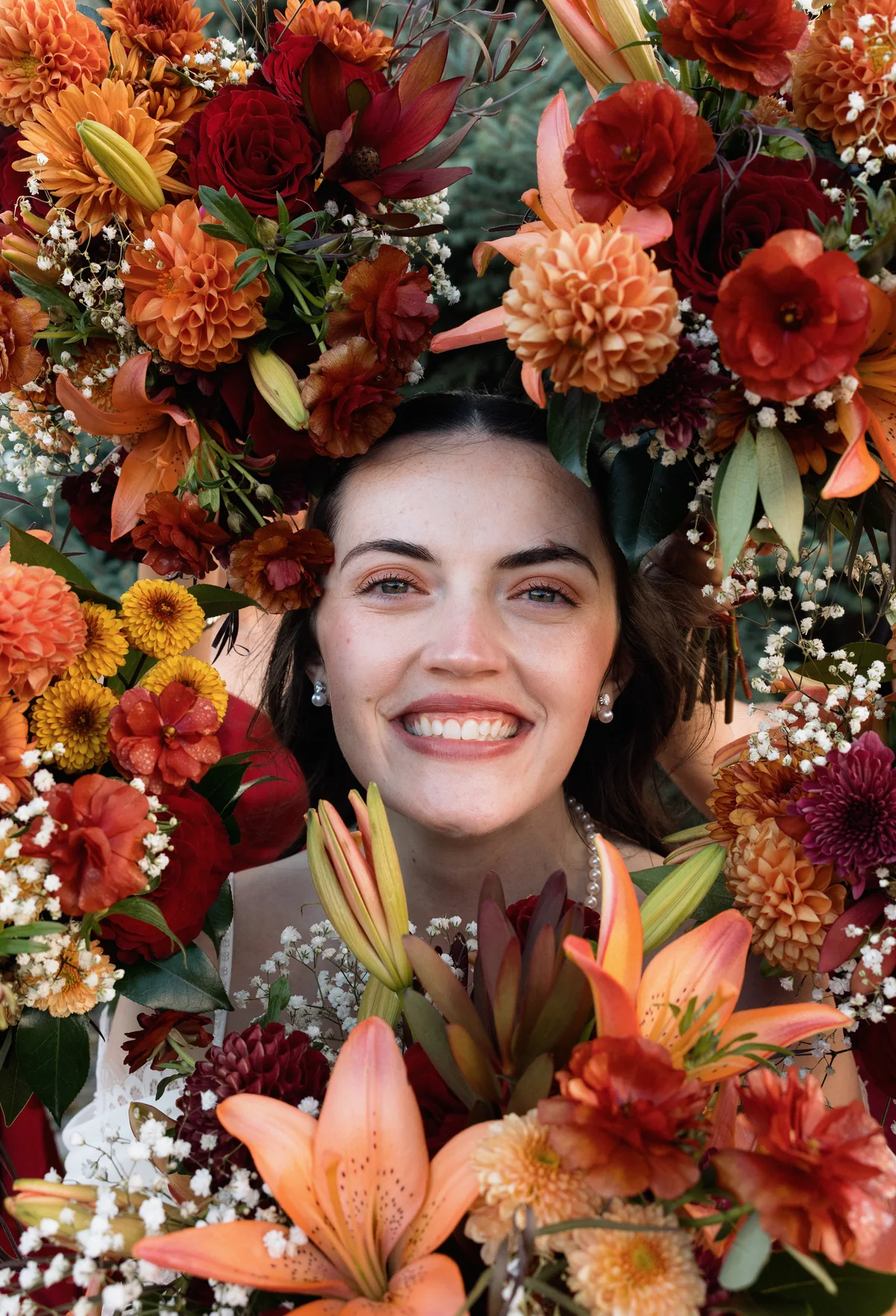 Bride smiling up through a ring of orange and red fall flowers