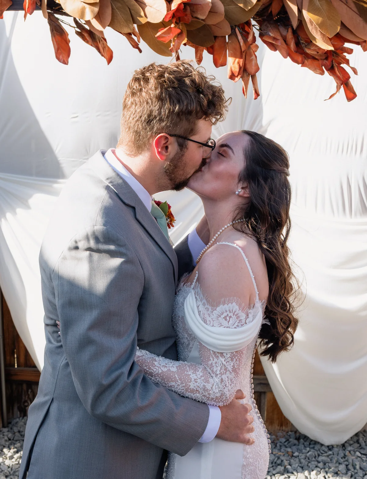 First kiss under a garland of copper leaves at a backyard ceremony
