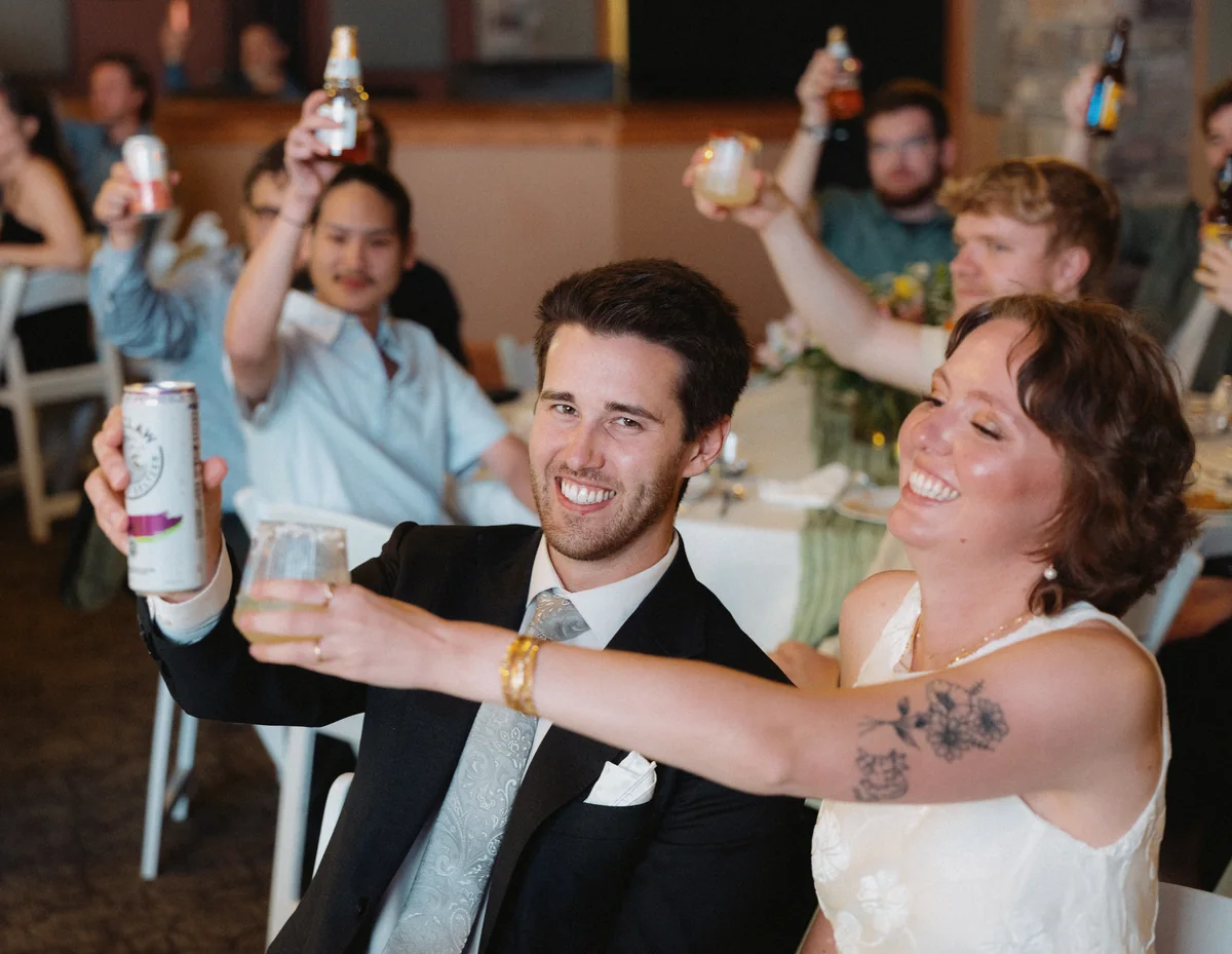 Newlyweds raising their drinks with friends during the reception toasts