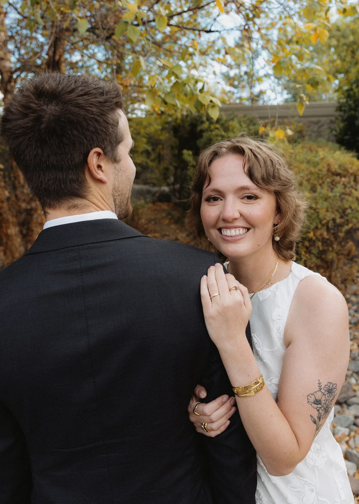 Bride smiling over the groom's shoulder among autumn trees