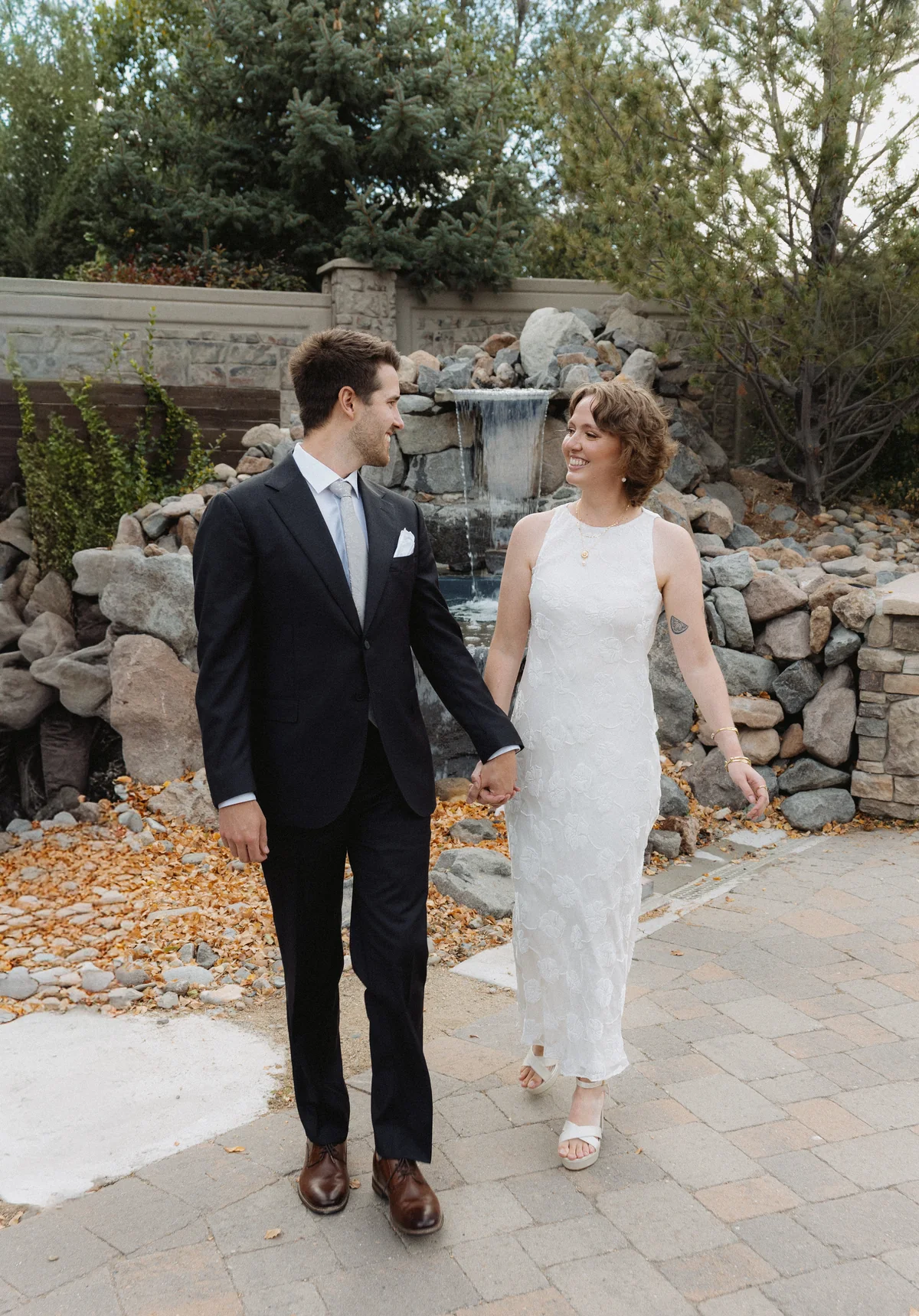 Bride and groom walking hand in hand on a stone path past a rock waterfall