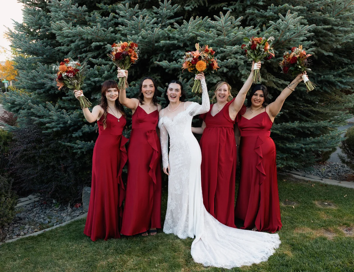Bride and her bridesmaids in red dresses raising their bouquets