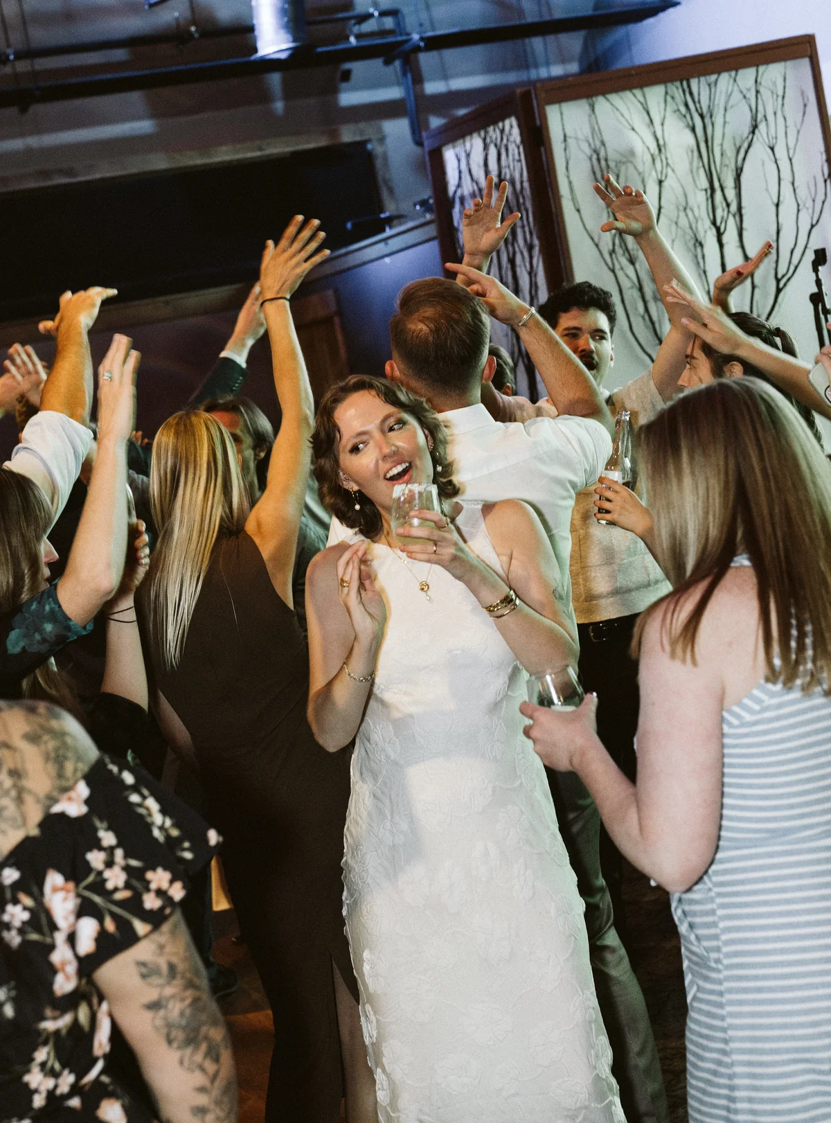 Bride dancing with her arms up in a crowded reception