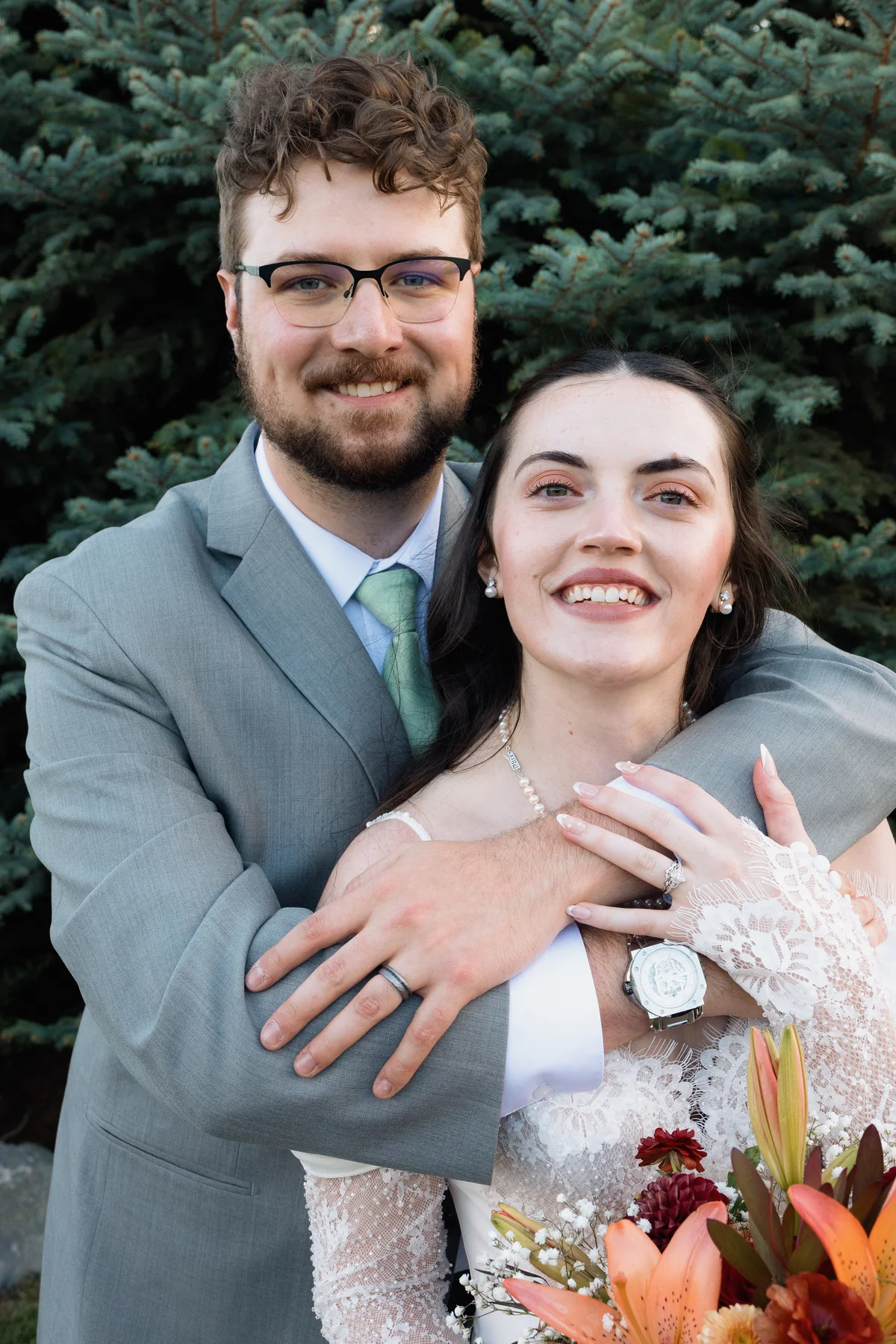 Groom hugging the bride from behind as both smile at the camera