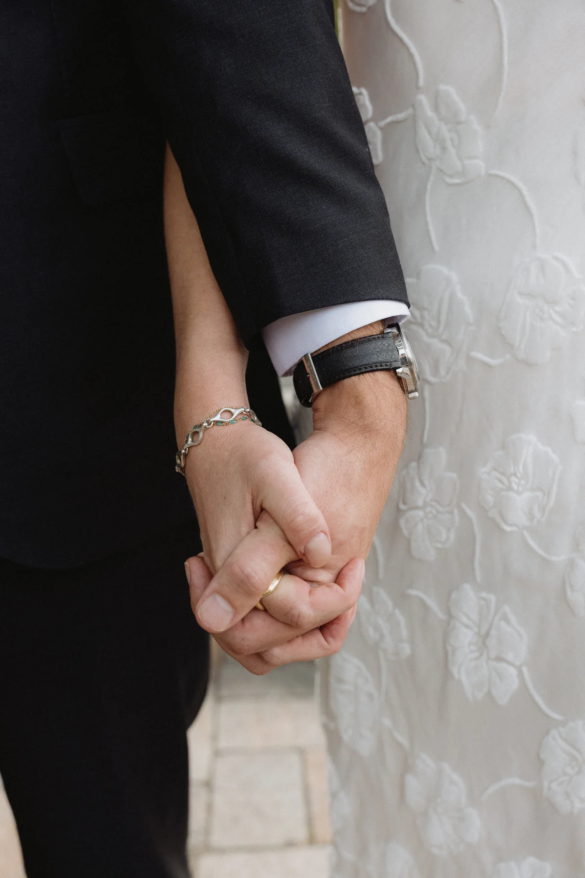 Close detail of the couple holding hands against her lace dress