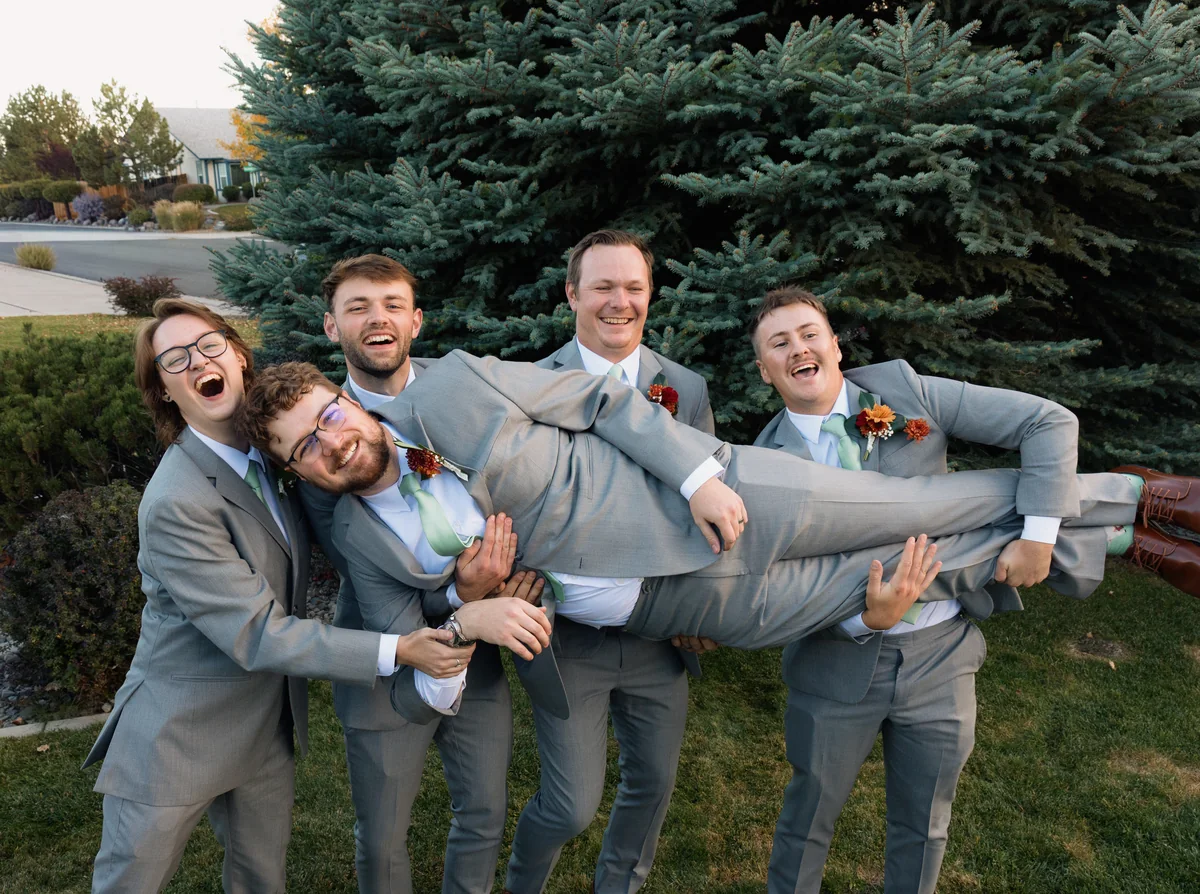 Groomsmen carrying the groom sideways and laughing