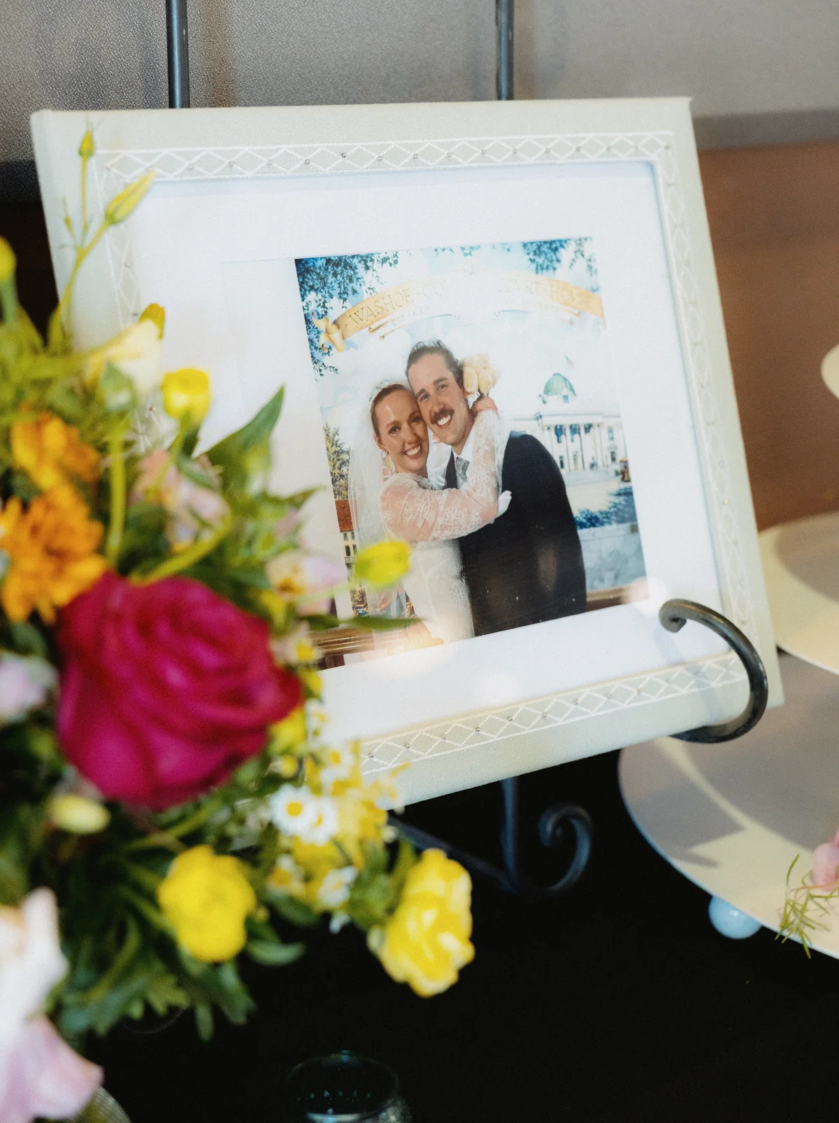 Framed photo of the couple beside a bright bouquet at the reception